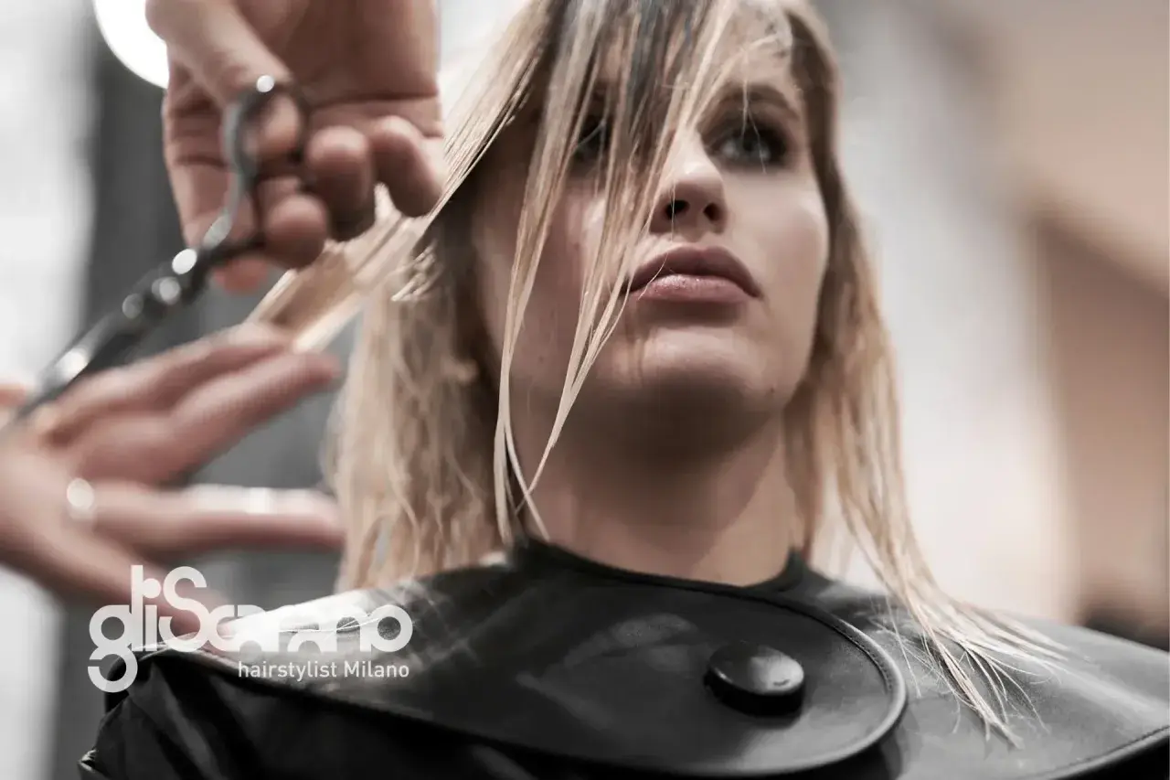 Un parrucchiere taglia i capelli biondi di una modella. La domanda "ogni quanto tagliare i capelli" è fondamentale per mantenere la chioma sana.