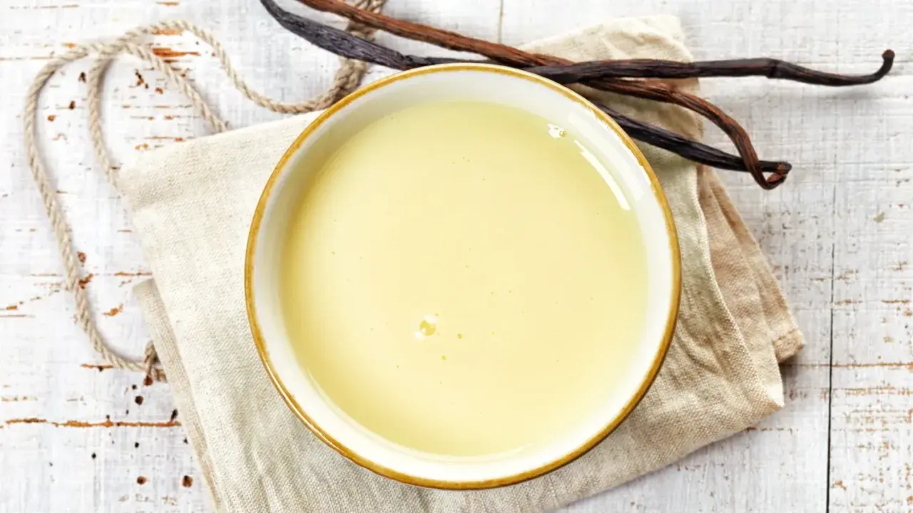 Un bol de crème anglaise onctueuse, prêt à être dégusté, avec des gousses de vanille à proximité.