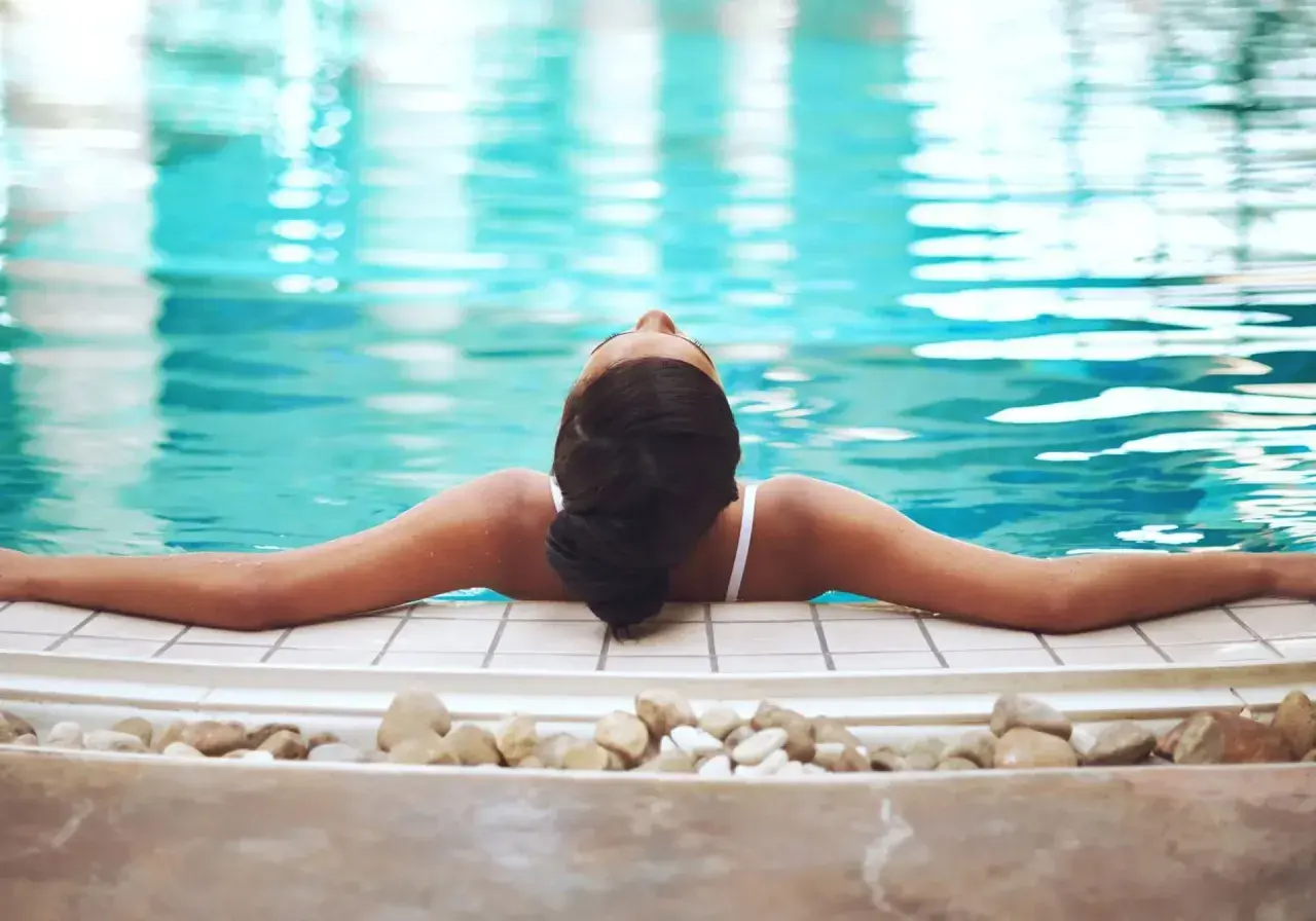Avslappnad kvinna njuter av ett spa i Tyskland, med armarna utsträckta över kanten av en turkos pool.