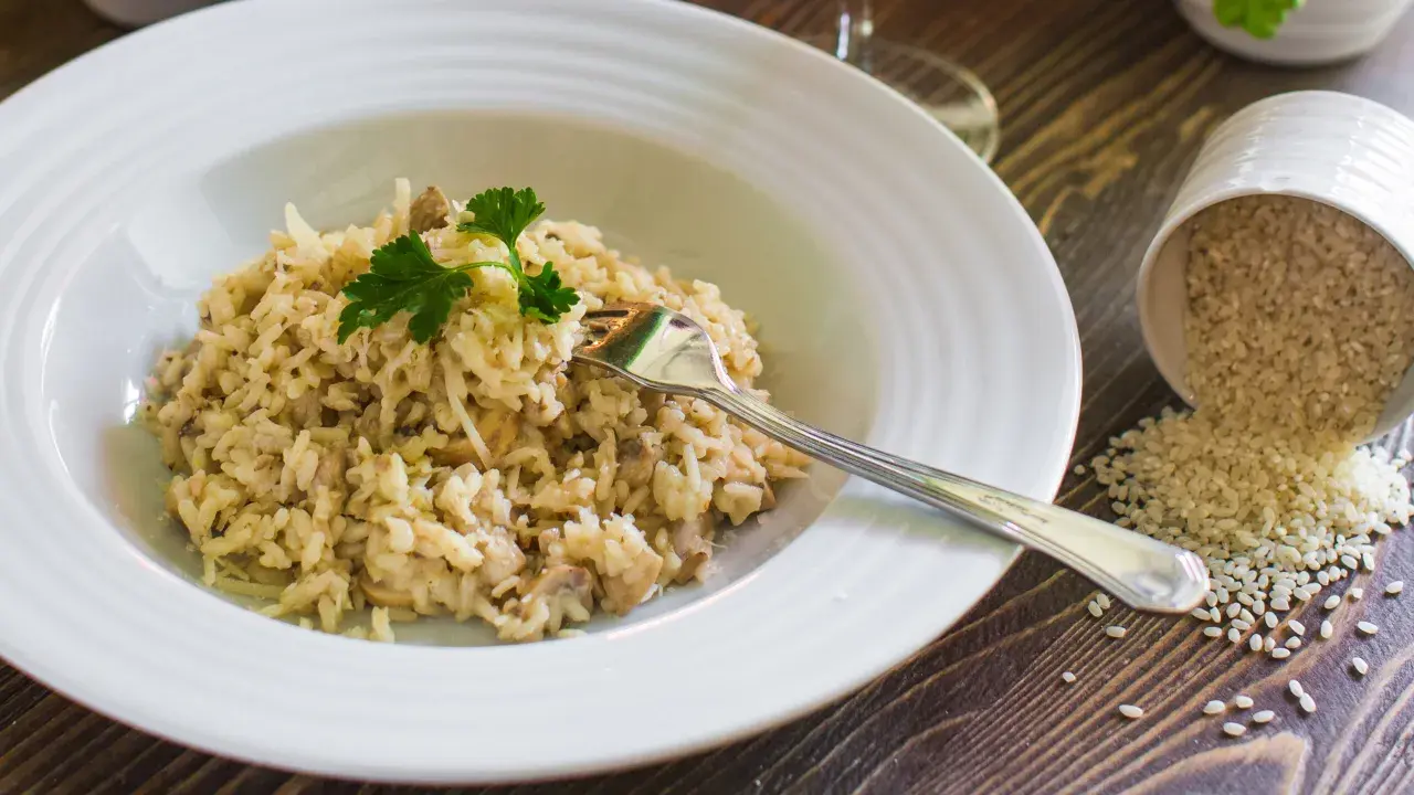 Un cremoso risotto con champiñones y queso parmesano, listo para disfrutar. Al lado, un cuenco volcado con arroz para risotto.