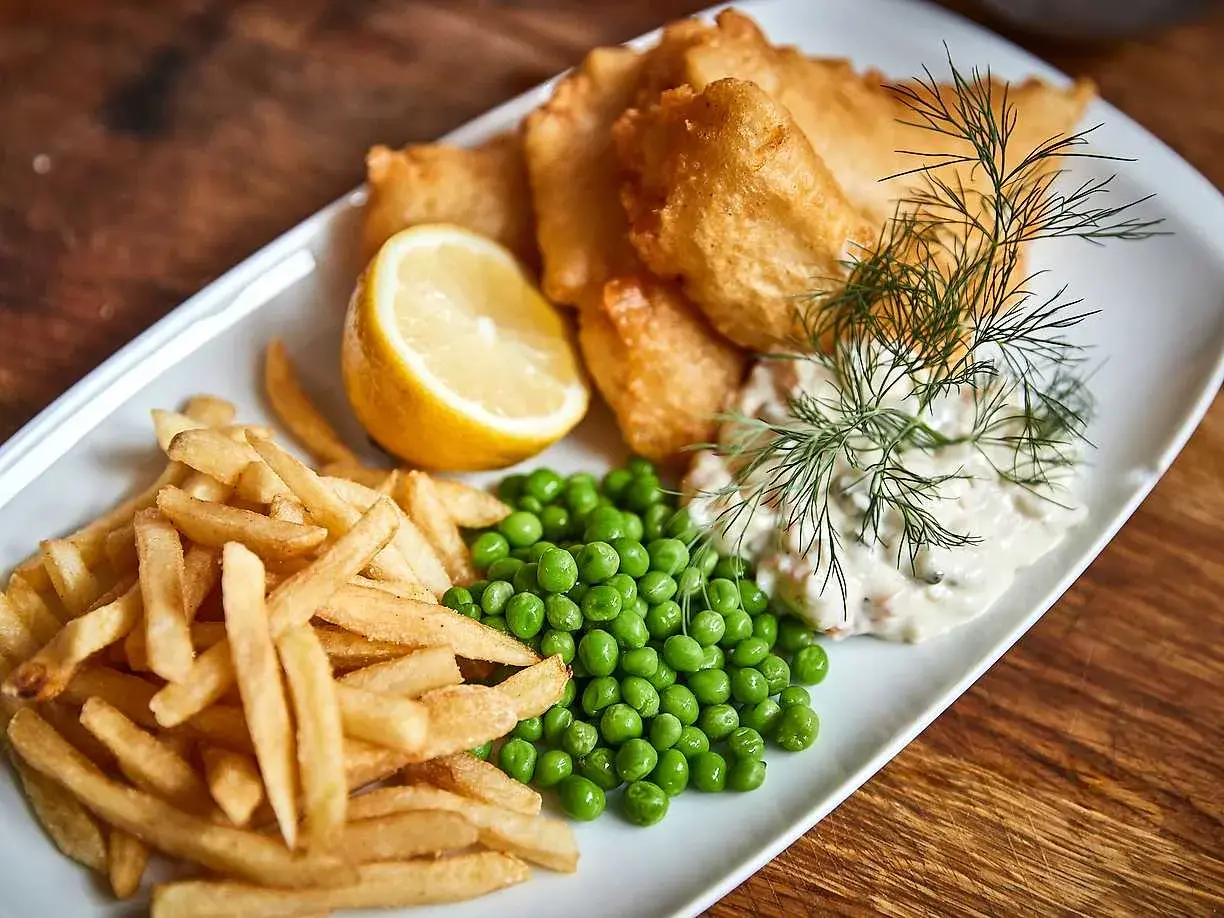 En tallrik med fish and chips, ärtor, citronklyfta och remouladsås.