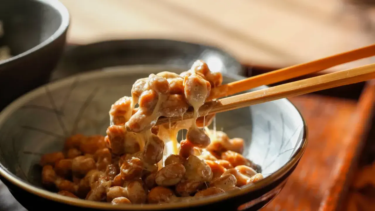 Natto chinasi: attenzione alle controindicazioni. Un primo piano di natto appiccicoso sollevato da bacchette.