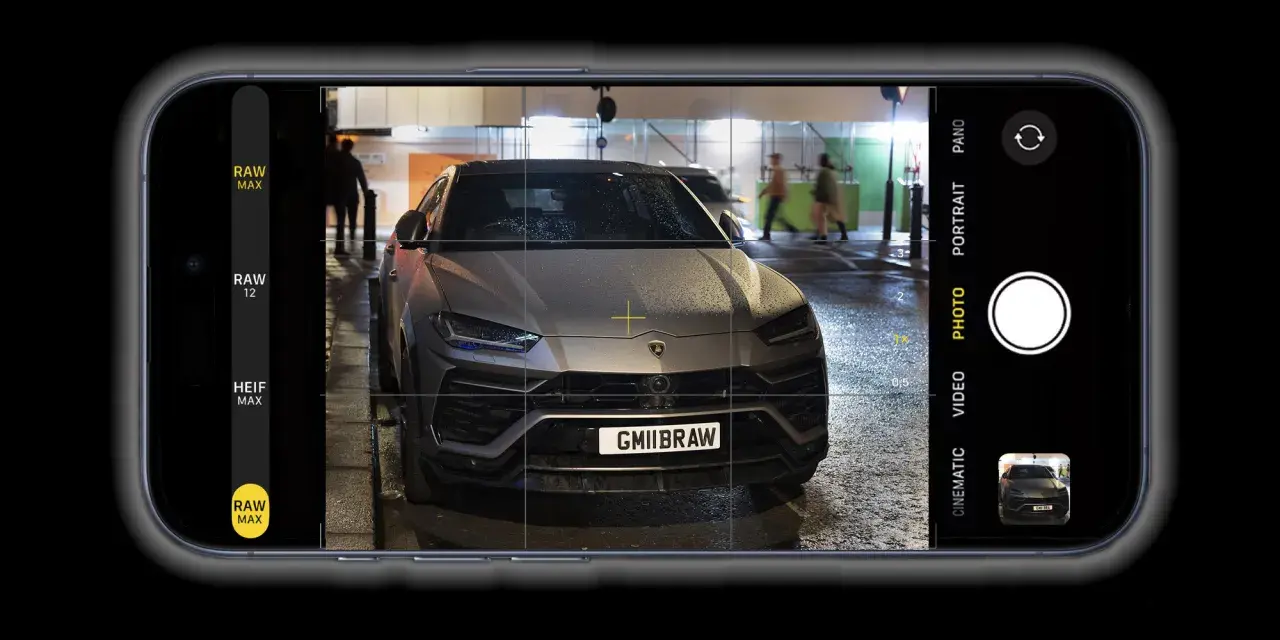 Un'auto sportiva grigia, con targa GMIIBRAW, inquadrata dall'app fotocamera di un iPhone con opzione apple proraw attiva.