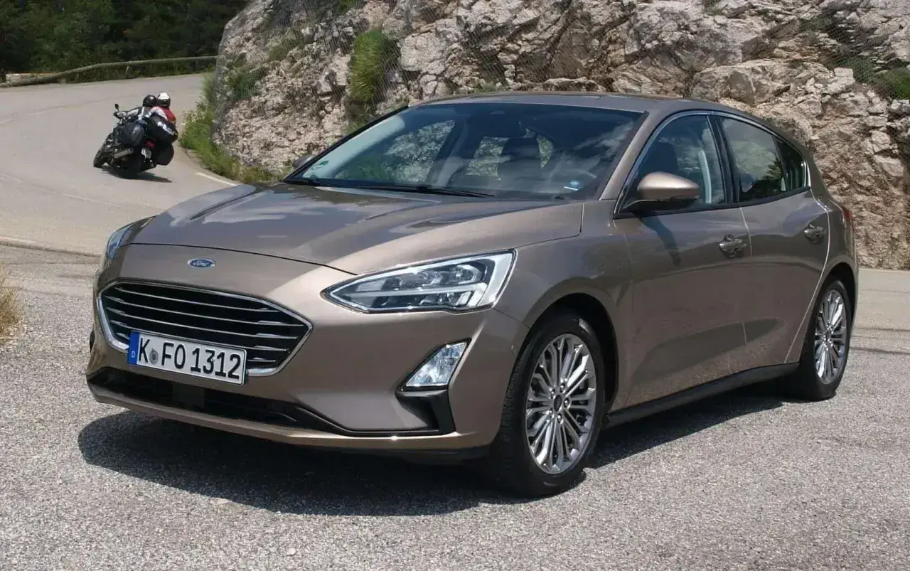 Brązowy Ford Focus MK3 1.6 TDCI na krętej drodze, z motocyklistą w tle.