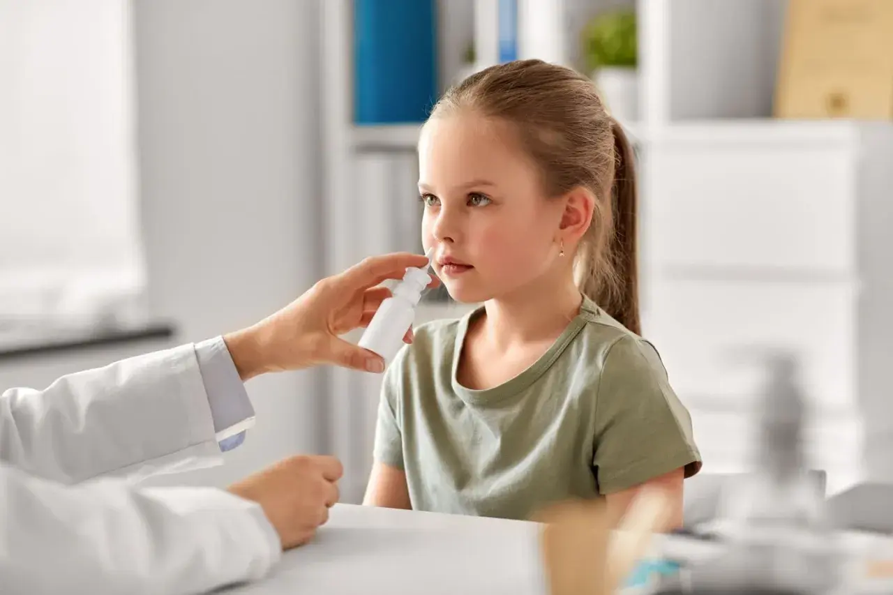 Niña recibe spray nasal para aliviar síntomas de rinitis alérgica. El doctor investiga las causas.