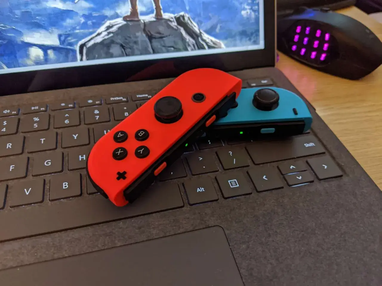 Czerwony i niebieski Joy-Con na klawiaturze laptopa, gotowe do gry. Dowiedz się, jak podłączyć Nintendo do komputera.