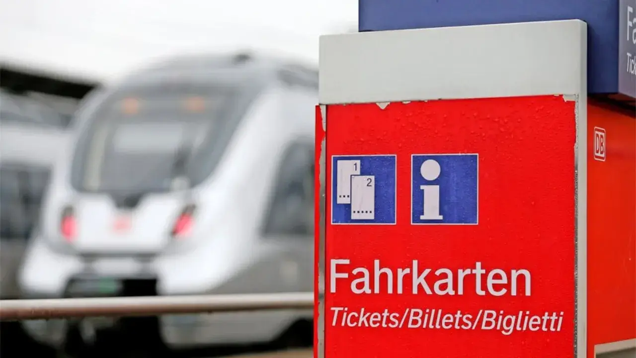Roter Fahrkartenautomat am Bahnhof. Ein Zug fährt vorbei. Wann am besten Bahntickets buchen? Hier gibt es Infos.