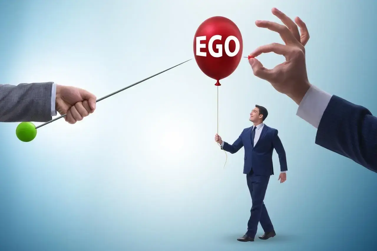 Mężczyzna z balonem "EGO" w ręku, symbolizujący cechy narcyza, zagrożony przez szpilkę.