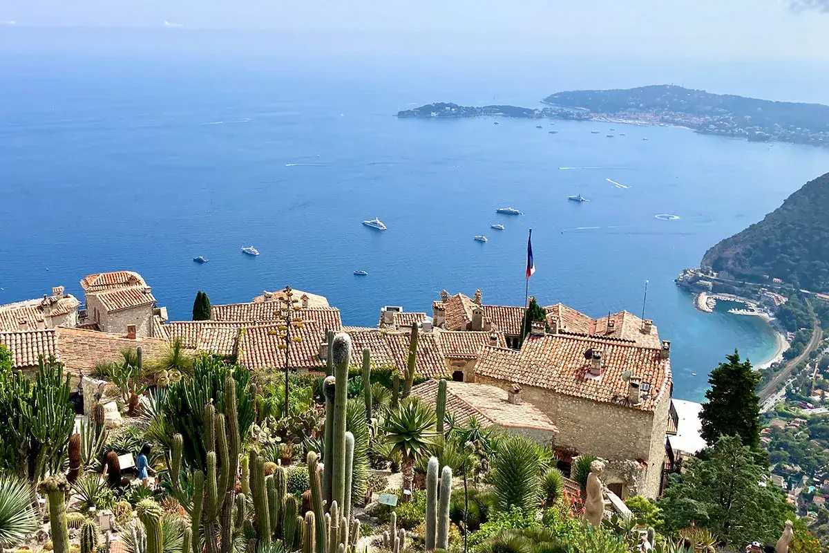 Ein malerischer Blick auf die **Côte d'Azur** mit einem Kakteengarten, alten Häusern und dem azurblauen Meer voller Yachten.