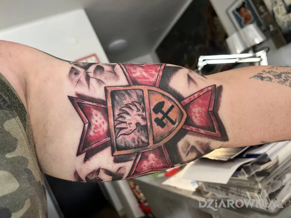 Tatuaż patriotyczny na ramieniu: lew w koronie i skrzyżowane młot i kilof na tle czerwonej gwiazdy.