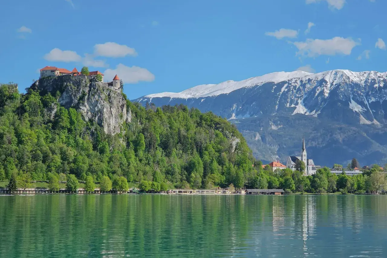 Blick auf die Burg von Bled über dem smaragdgrünen See, mit schneebedeckten Bergen im Hintergrund.