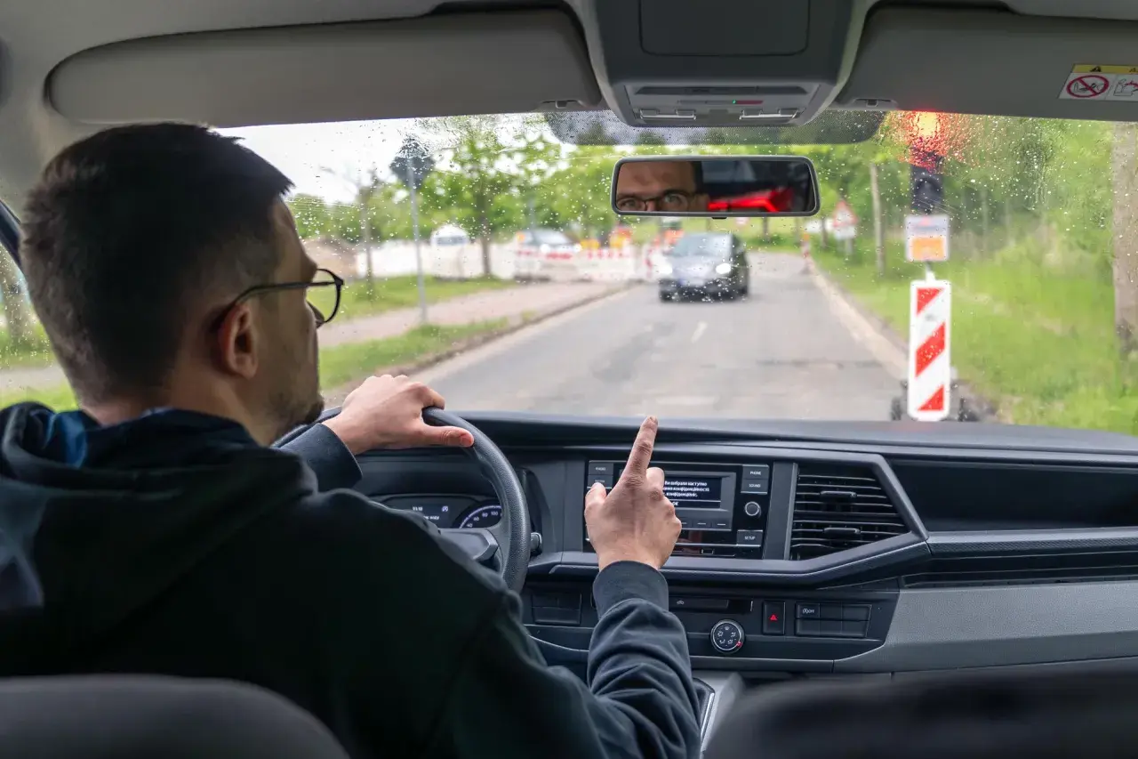 Kierowca w okularach wskazuje palcem na ekran nawigacji, gdy zbliża się do drogi dla pieszych.
