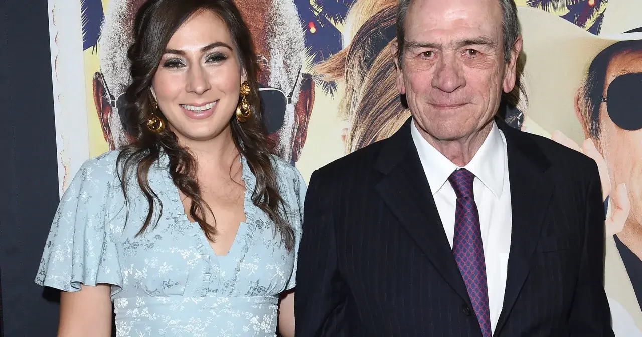 Tommy Lee Jones z żoną, uśmiechnięci na tle plakatu filmowego.