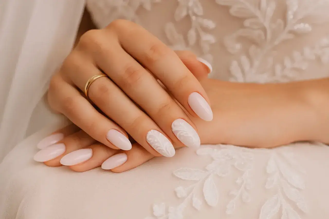 Mains d'une mariée aux ongles pastel ornés de dentelle blanche, parfaits pour un mariage.