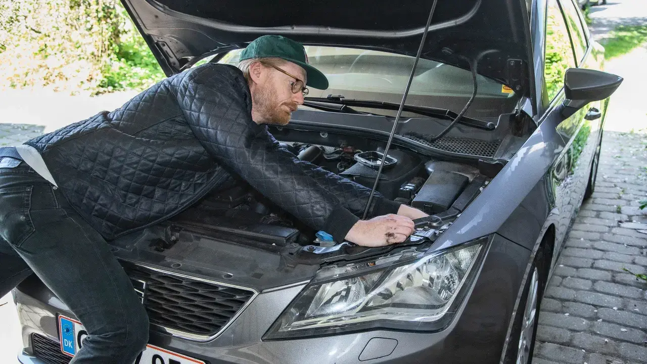 Man med keps och glasögon böjer sig över motorhuven för att byta halogenlampa.