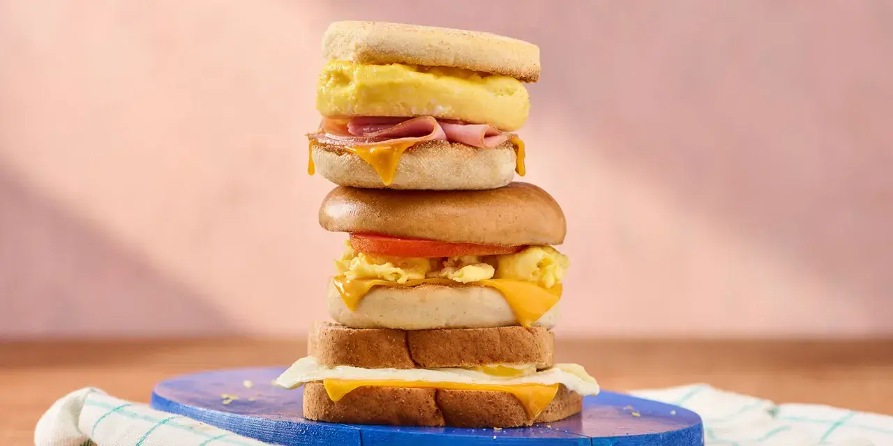 Une pile de sandwichs gourmands, parfaits pour une recette de petit-déjeuner. Œufs brouillés, fromage fondant, jambon et tomate.
