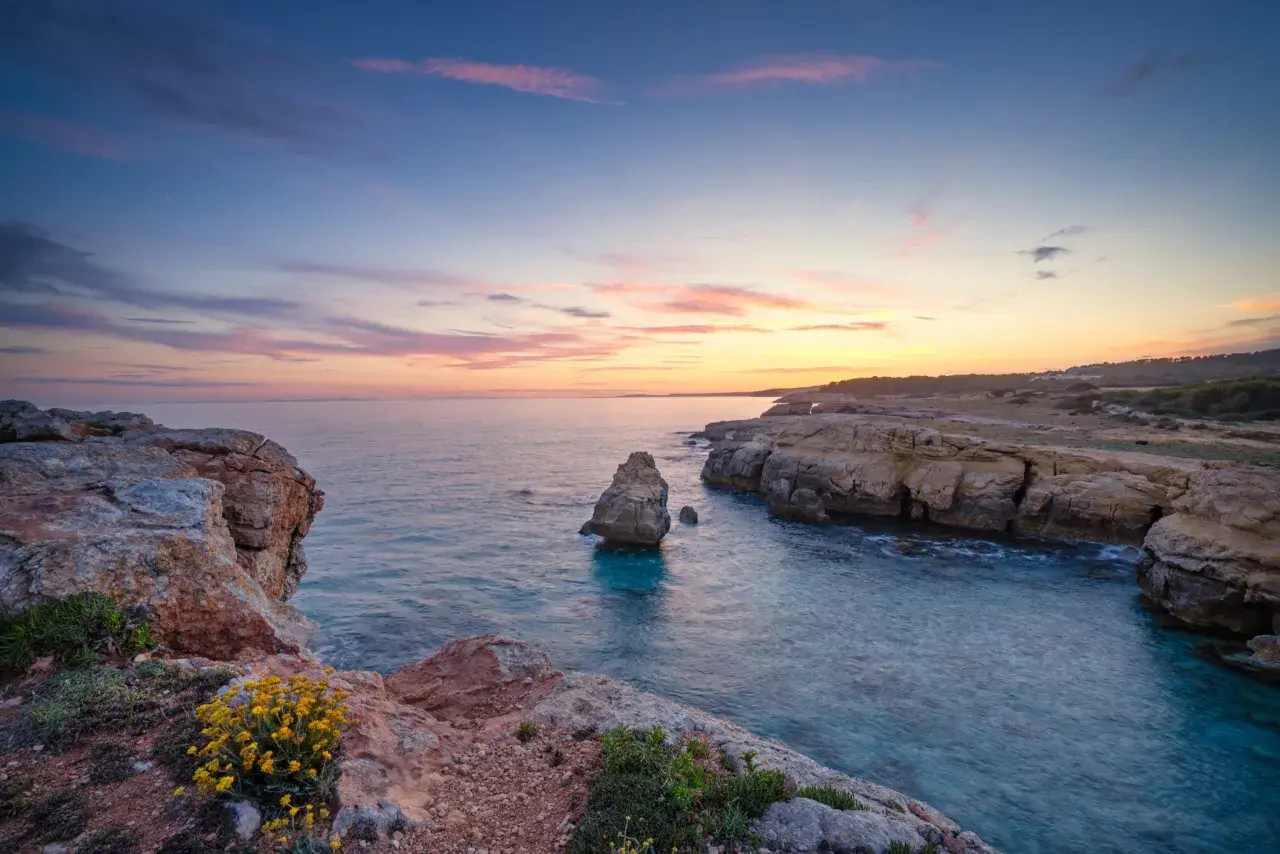 Sonnenuntergang an Menorcas Küste. Felsen, türkises Wasser und ein pastellfarbener Himmel – perfekte Menorca Urlaub Tipps für Romantiker.