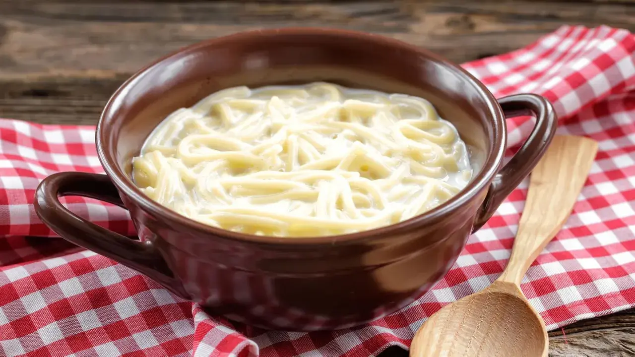Eine Schüssel mit milch nudeln, serviert auf kariertem Stoff. Ein Holzlöffel liegt daneben.