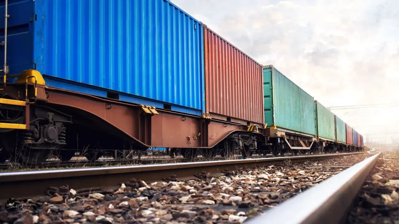 Długi pociąg towarowy z kolorowymi kontenerami na torach. To przykład transportu kolejowego, który jest kluczowy dla globalnej logistyki.