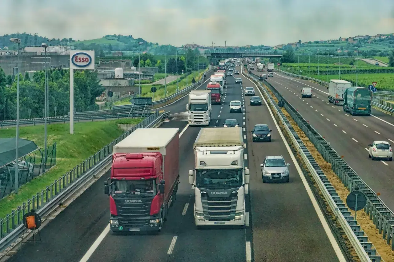Kierowca zawodowy w trasie, ciężarówki na autostradzie. W tle znak Esso i zielone wzgórza.