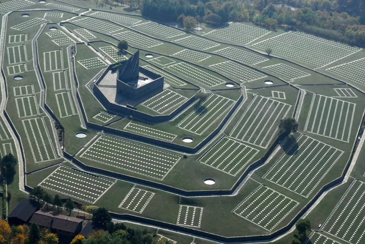 Vista aerea del cimitero tedesco al Passo della Futa, con file ordinate di croci bianche su prati verdi e un imponente monumento centrale.