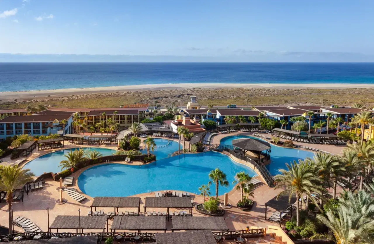 Ein Urlaubsparadies am Meer: Große Poollandschaft mit Palmen und Liegen, dahinter das Robinson Jandia Playa Resort und der weite Sandstrand.