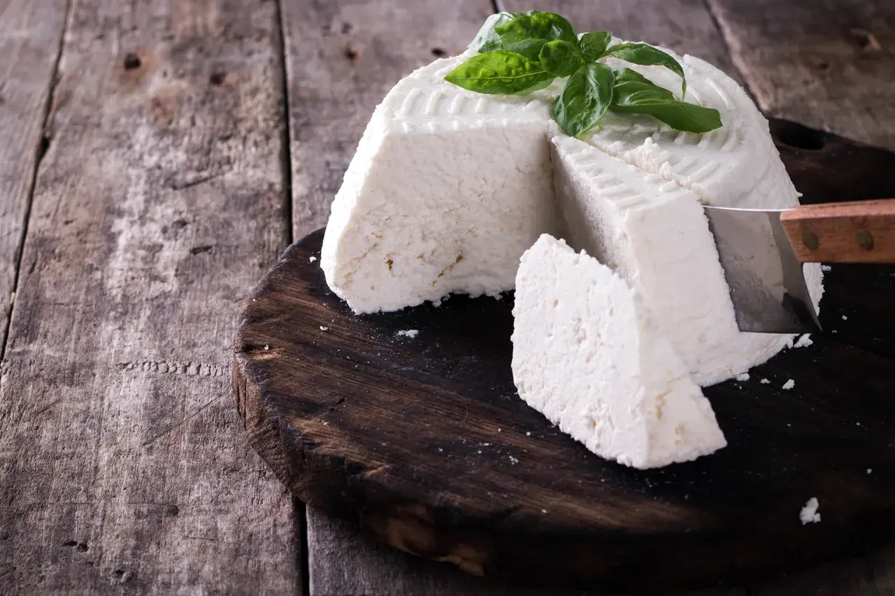Ricotta fatta in casa, fresca e profumata, guarnita con basilico, pronta per essere gustata su un tagliere di legno rustico.
