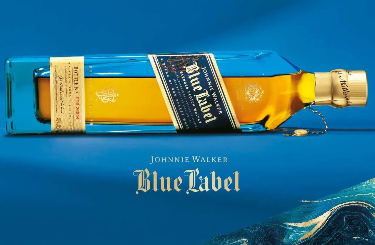 Elegancka butelka Johnnie Walker Blue Label leży na niebieskim tle. Złoty płyn i niebieskie szkło tworzą luksusowy kontrast.