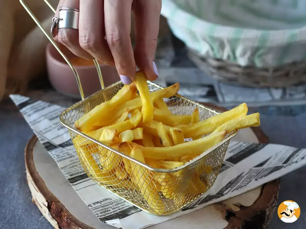 En hand plockar upp en gyllene pommes frites ur ett korgfat. Perfekt för en snabb aptitretare.