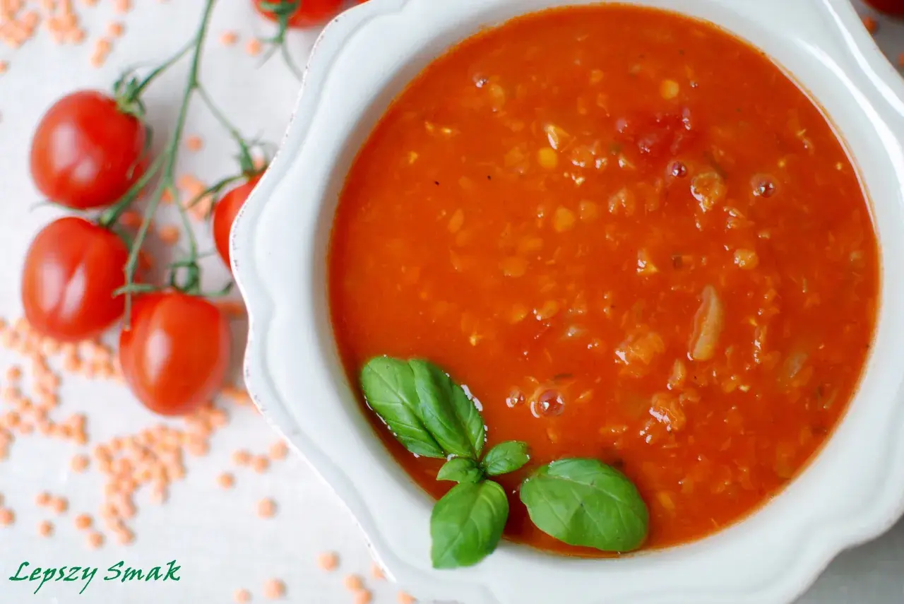 Zupa pomidorowa z soczewicą, ozdobiona bazylią. Obok gałązka pomidorków i rozsypana soczewica. Idealna na chłodne dni, smakuje jak domowe pesto pomidorowe.