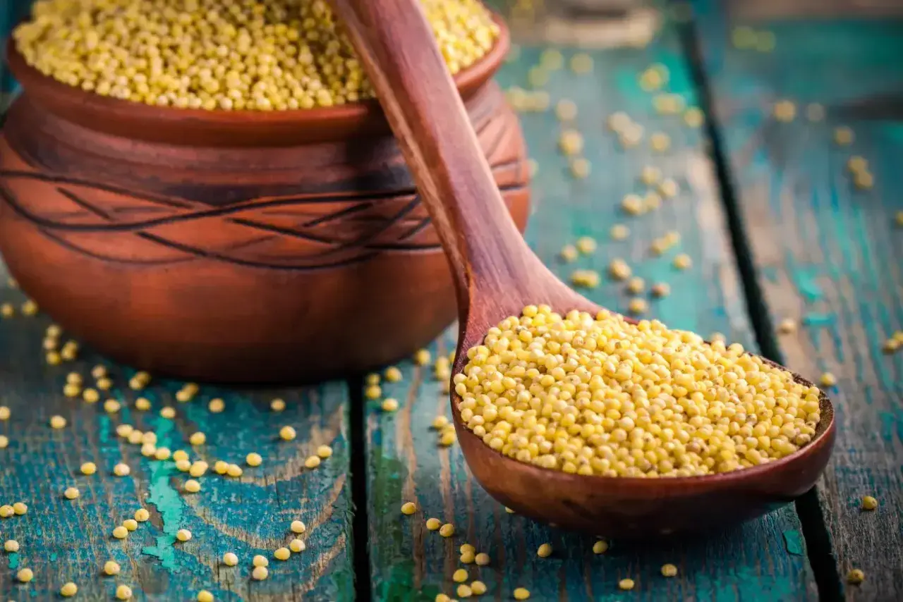 Kasza jaglana na drewnianej łyżce, obok glinianego naczynia. Niska wartość indeksu glikemicznego sprawia, że jest zdrowym wyborem.