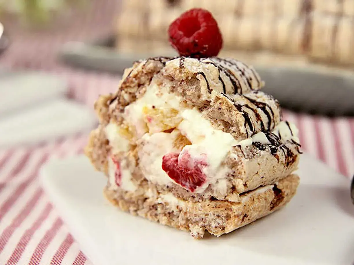 En läcker budapestbakelse med vispgrädde, frukt och chokladdrizzle, toppad med ett hallon.