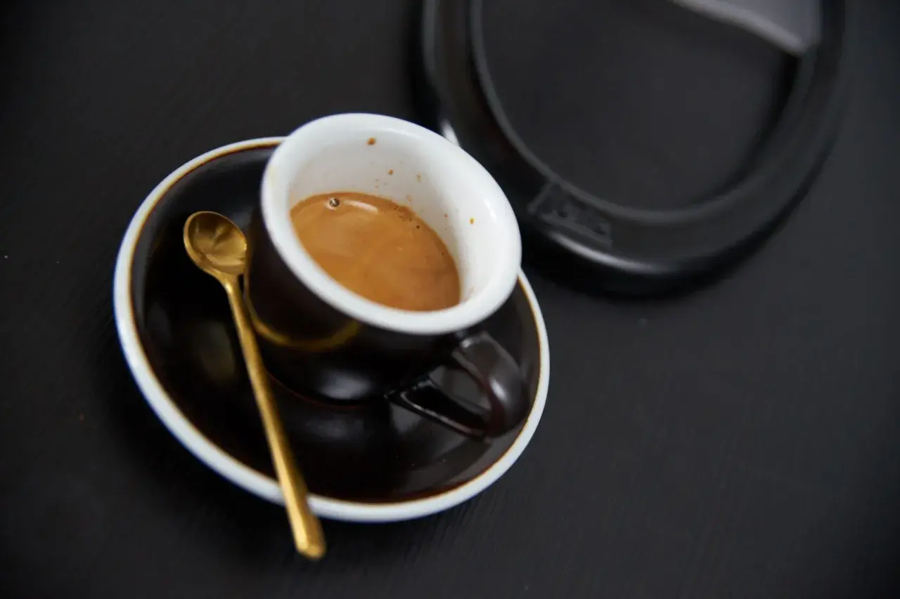 Aromatyczne włoskie espresso w filiżance z złotą łyżeczką na czarnym tle. Idealny początek dnia.