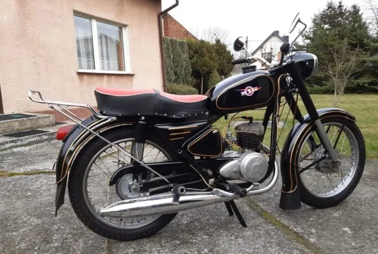 Czarny motocykl WSK z czerwoną kanapą i złotymi ozdobami, stojący na podjeździe.