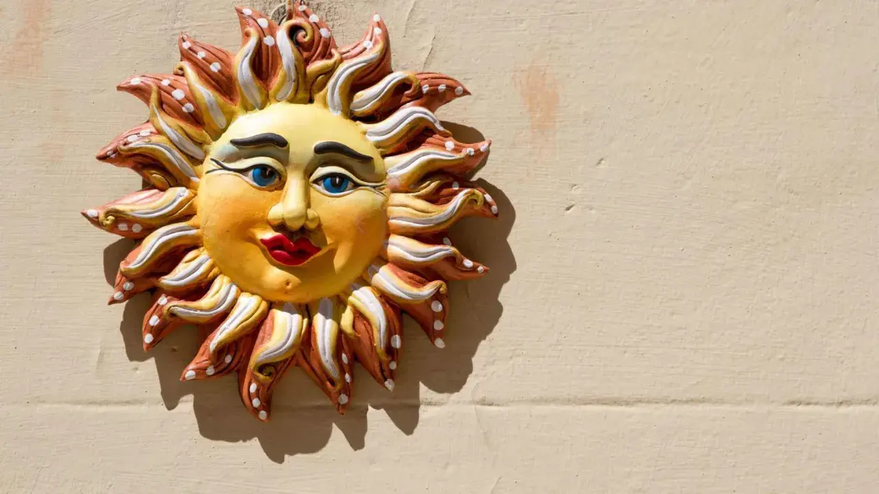 Sole decorativo in ceramica, un esempio di artigianato italiano, con volto sorridente e raggi colorati su muro beige.