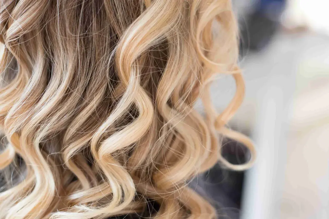 Falowane blond włosy z jaśniejszymi pasemkami, tworzące naturalne rozświetlenie.