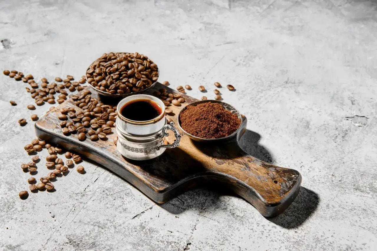 Chicco di caffè, macinato e bevanda scura su tagliere rustico. Chi dice che il caffè fa male, non ha visto questa meraviglia.