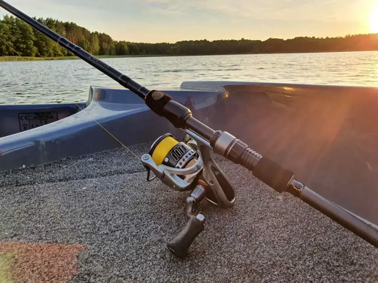 Wędka na sandacza gotowa do akcji na spokojnym jeziorze o zachodzie słońca. Idealny sprzęt na łowienie drapieżników.