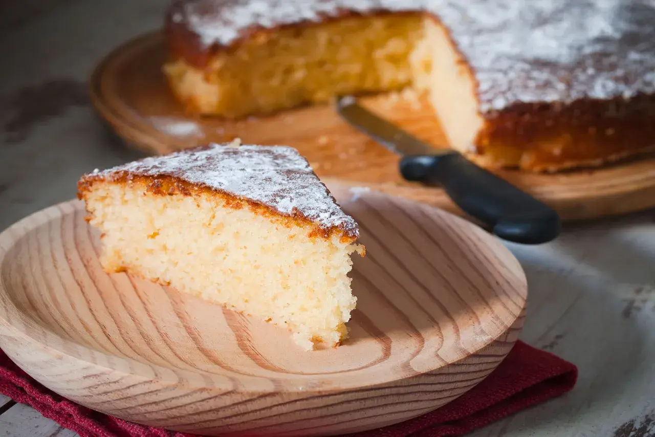 Una fetta di torta all'acqua soffice e spolverata di zucchero a velo su un piatto di legno.