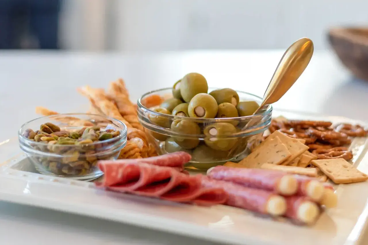 Plateau apéro raclette : olives, pistaches, salami, bretzels et crackers. Parfait pour un moment convivial.