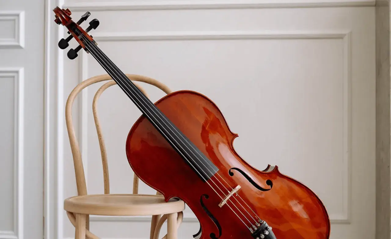 Un magnifique violoncelle en bois verni repose sur une chaise en bois clair, prêt à faire vibrer ses cordes.