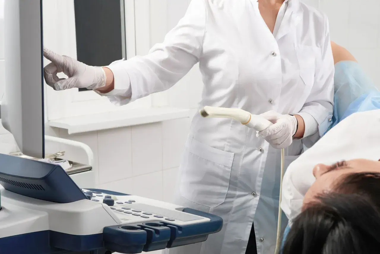 Arzt führt eine Untersuchung mit einem Ultraschallgerät durch. Die Patientin liegt auf dem Tisch.