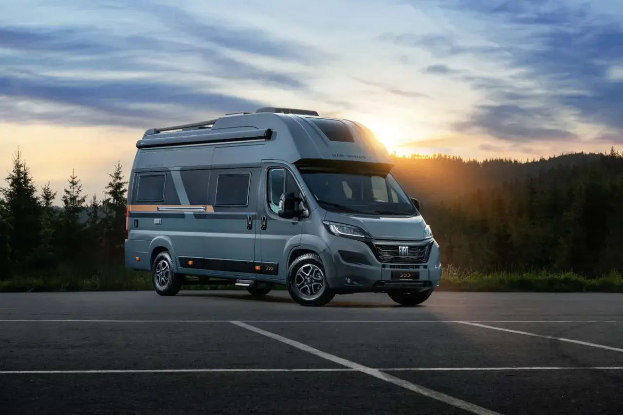Nowe kampery Globe Traveller zapraszają na przygodę. Szary Fiat Ducato z nowoczesnym designem na tle zachodzącego słońca i lasu.