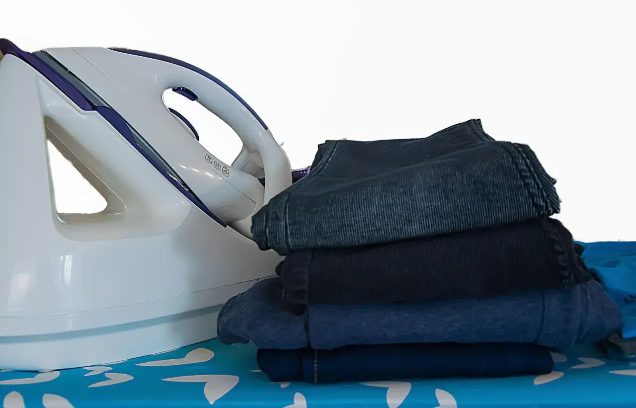 Fer à repasser et pile de vêtements sombres sur une planche à repasser. Apprenez comment repasser du polyester pour un résultat impeccable.