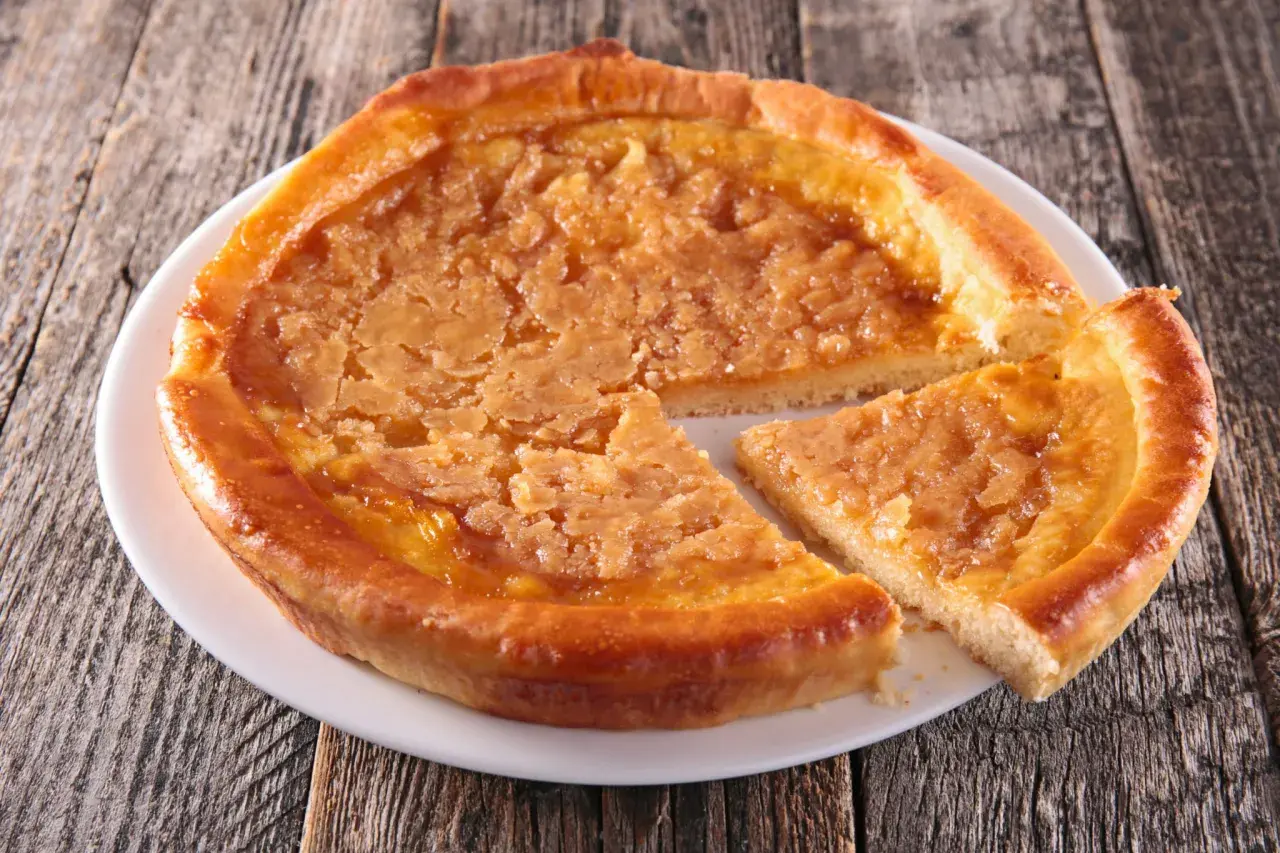 Une tarte au sucre dorée, avec une tranche coupée, sur une assiette blanche posée sur un fond en bois rustique.