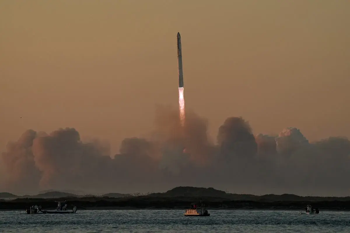 Starship start. Rakieta wznosi się w niebo, zostawiając za sobą kłęby dymu. Na wodzie widać łodzie obserwujące ten spektakularny widok.