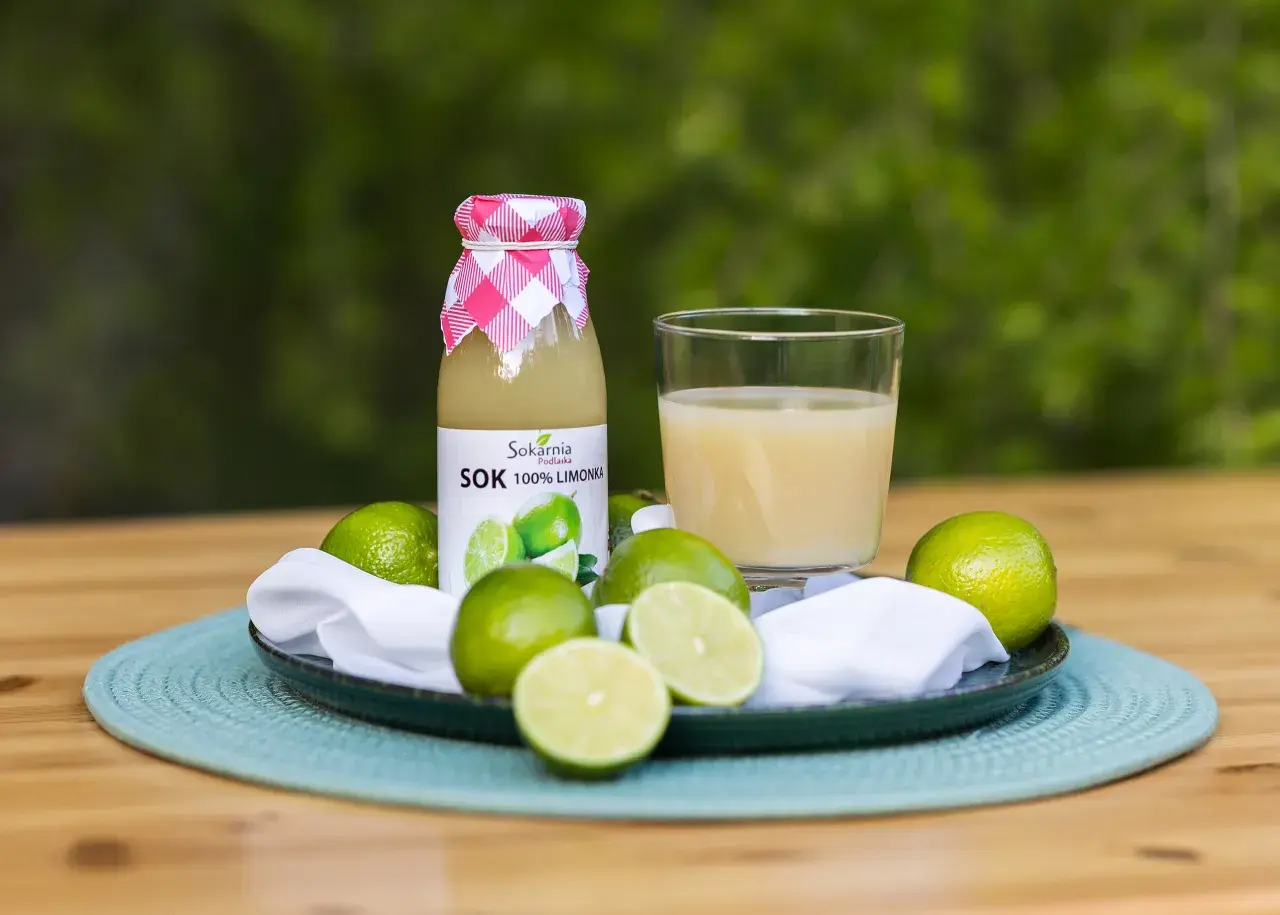 Butelka soku z limonki i szklanka orzeźwiającego napoju, otoczone świeżymi owocami. Odkryj sok z limonki właściwości!