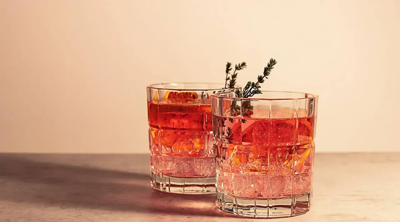 Dwa drinki z plasterkami pomarańczy i gałązkami ziół w szklankach z grubego szkła. Idealne na letni wieczór, dodają klimatu.