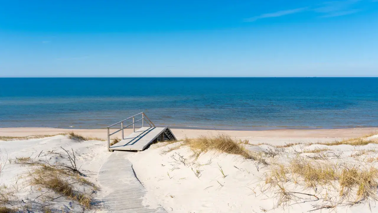 Drewniane schody prowadzą na piaszczystą stegna plaża. Błękitne morze i niebo tworzą spokojny krajobraz.