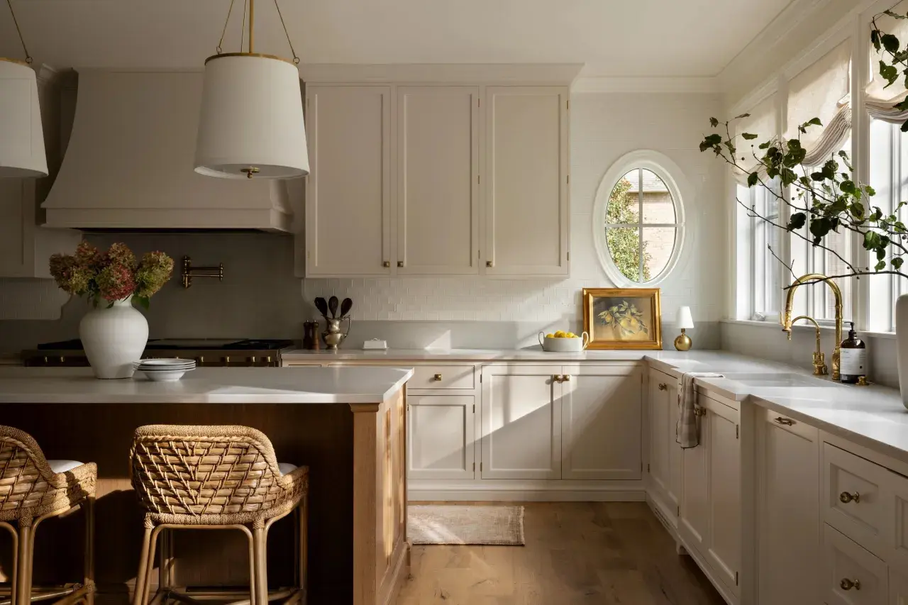 A bright, airy Studio McGee kitchen with cream cabinetry, a large island, woven stools, and a charming oval window.